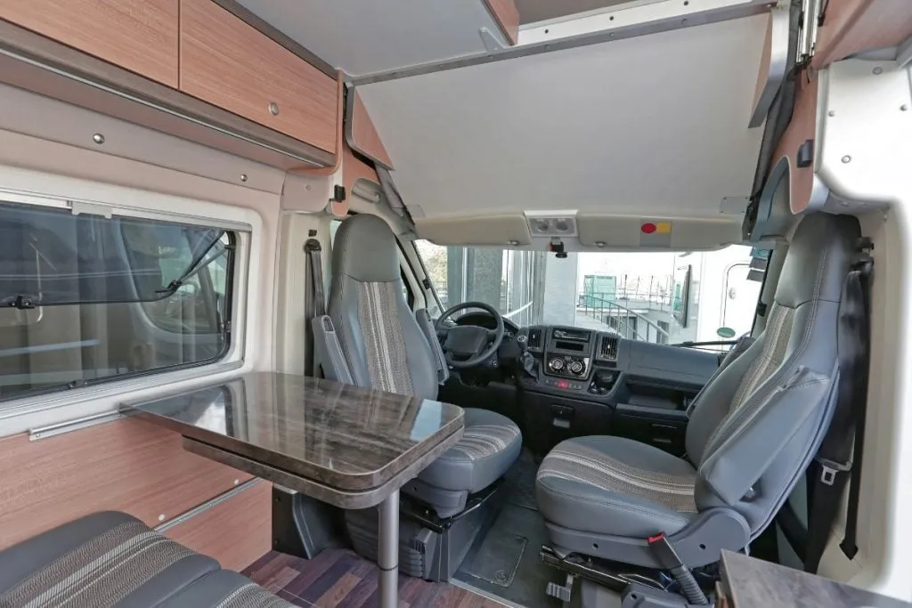 The cab of a campervan seen from the living area, with swivelling front seats and a small dining table