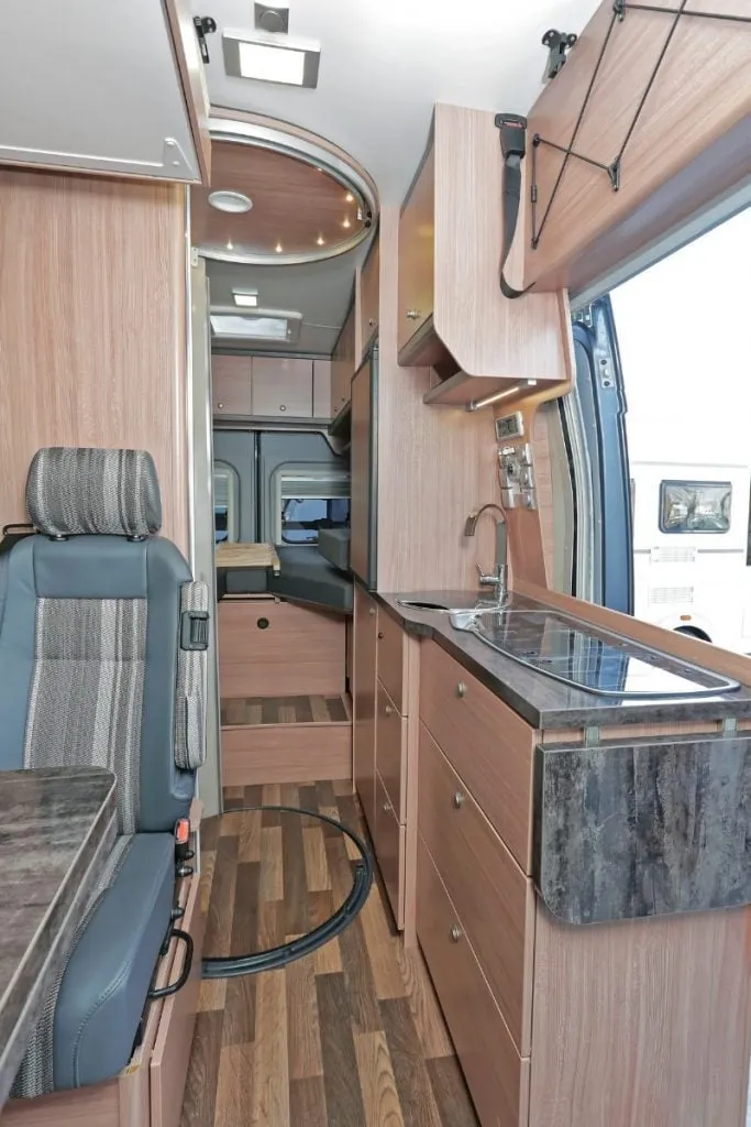 A campervan interior looking down the galley kitchen past a swivel seat to the rear bed