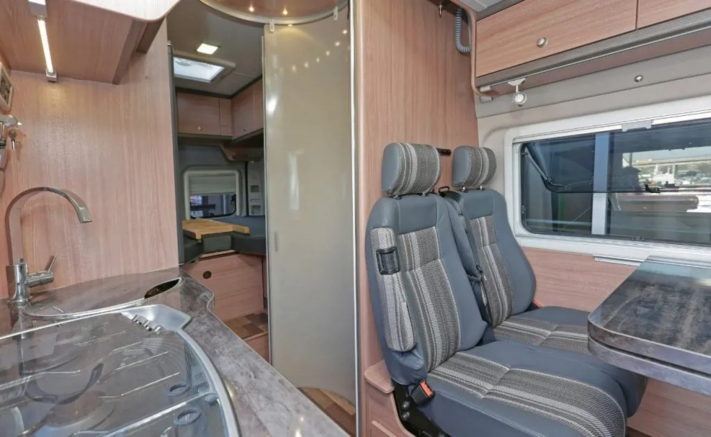 A campervan kitchen and dining area with a sink, benchtop and two travel seats, looking through to the rear bed