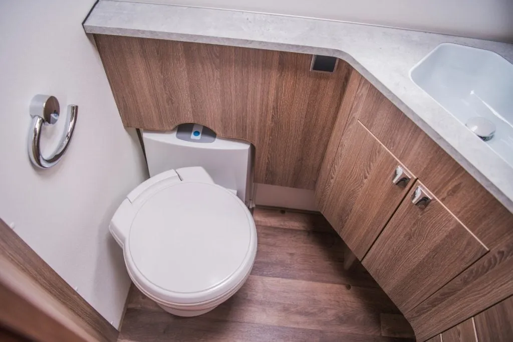 A campervan washroom with a swivel-cassette toilet, timber cabinetry and a corner basin