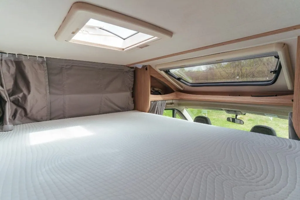 A made-up double bed in a motorhome's over-cab cabin, with a skylight and a curtain to the living area