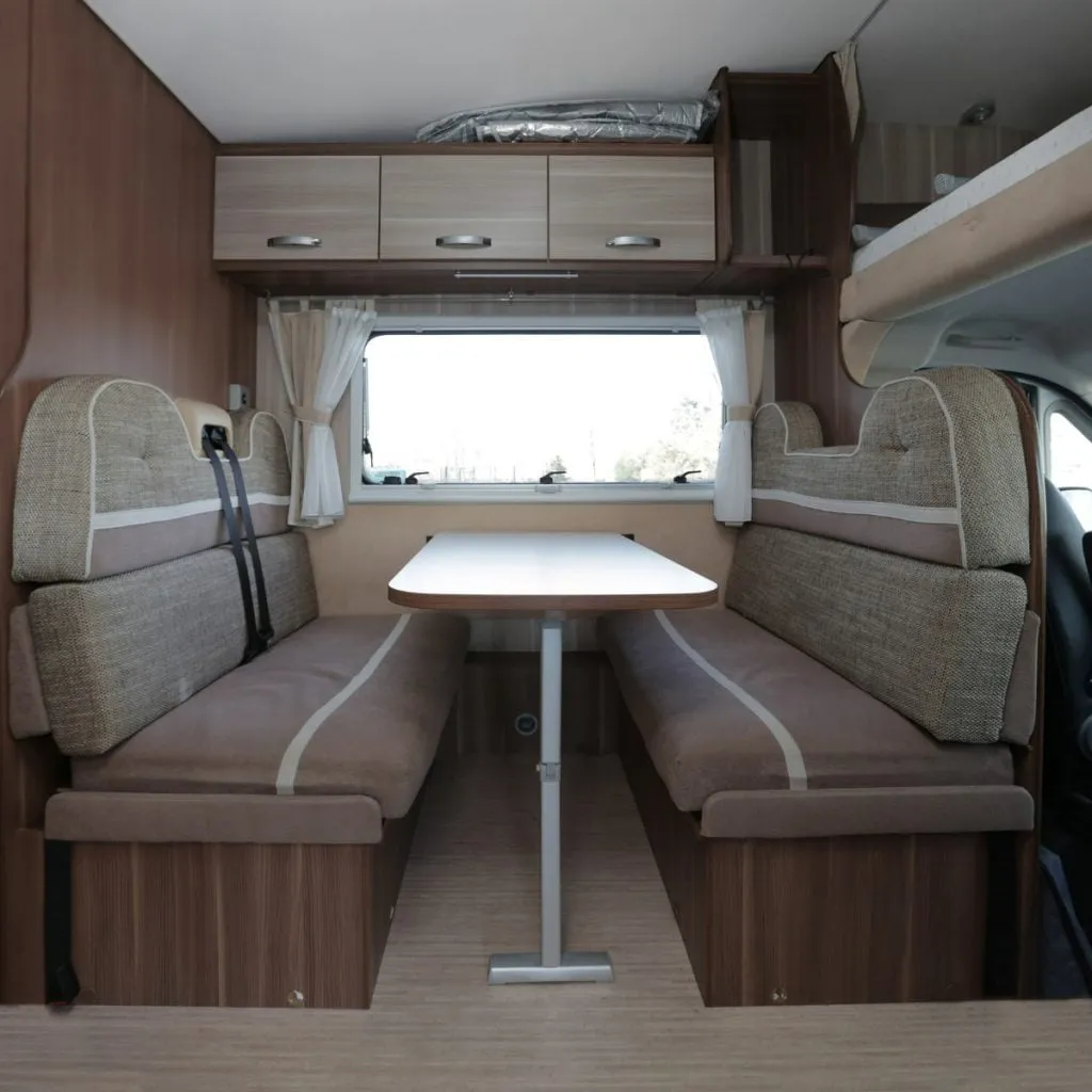 A motorhome dining area with two facing bench seats, a pull-up table and a bed stowed overhead