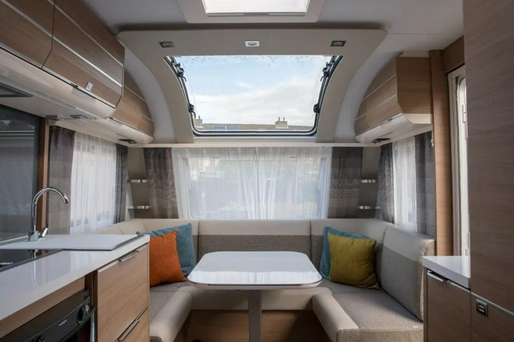 A motorhome kitchen and lounge with a U-shaped dinette, table, sink and overhead lockers under a large skylight