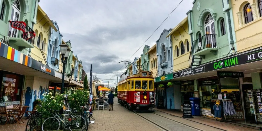 A city tour tram passing pastel-coloured shops and cafes on a Christchurch street
